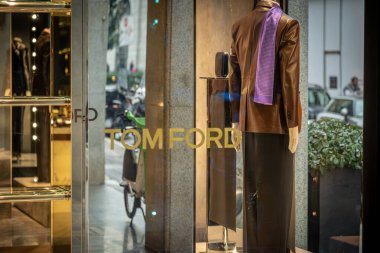 Milan, İtalya - 2026, 3 Şubat: Tom Ford FW25 butik vitrin vitrininde kahverengi deri ceketli ve mor atkılı şık bir manken, lüks moda eğilimlerini vurguluyor
