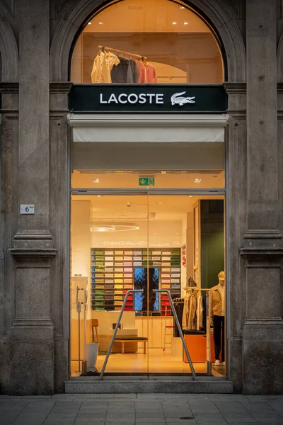 Milan, İtalya - 2026, 3 Şubat: Zarif taş cepheli Lacoste FW25 butiği, modern cam girişi ve şık bir şehir ortamında aydınlatılmış moda gösterileri