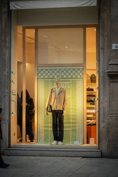 Milan, İtalya - 2026, 3 Şubat: Lacoste FW25 vitrin vitrininde şık, modern bir vitrinde yeşil tasarımcı arka planı ve modaya uygun şehir modasına sahip şık bir manken yer alıyor