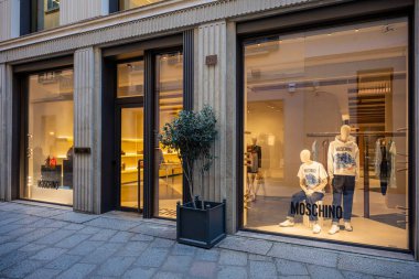 Milan, İtalya - 2026, 17 Şubat: Moschino SS26 butik vitrininde lüks moda eğilimlerini ön plana çıkaran modern, aydınlatılmış bir mağaza vitrininde şık tasarımcı kıyafetleri sergileniyor