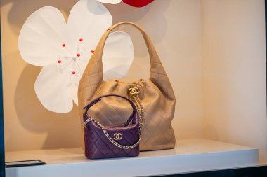 Milan, İtalya - 2026, 17 Şubat: Chanel SS26 altın ve simgesel logolu mor deri çantalar, çiçekli dekoru olan şık bir butik vitrinde sergileniyor