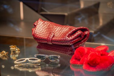 Milan, İtalya - 2026, 17 Şubat: Bottega Veneta SS26 kırmızı dokunmuş deri çanta, altın mücevher ve şık güneş gözlükleri modern bir butik ortamında sergilenmektedir.