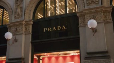 Milan, İtalya - 2026, 17 Şubat: Prada SS26 mağaza önü zarif mimari, altın logo ve canlı pencere ışıklandırmasıyla parlıyor, Milano 'da lüks modanın özünü yakalıyor