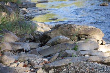 Bestrytsia riverbank with large and small rocks. Some sharp, others rounded. Water blue with yellowish reflections, calm among the stones.