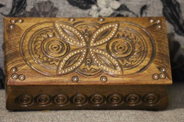 Christmas wooden box with intricate hand-carved lid patterns. Spiral and floral motifs, textile background blurred for focus on craftsmanship.