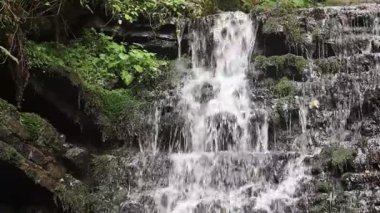 Şelale kayalık bir yamaçtan aşağı akar, sis yaratır ve su sıçratır. Çevreleyen doğa ihtişam hissi katıyor..