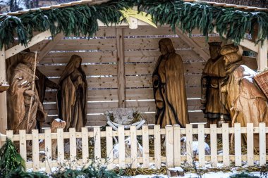 Güzel oyulmuş bir ahşap doğum sahnesinde kutsal aile ve bilge adamlar daimi yeşil dallar ve kayan yıldızlarla süslenmiş bir ahırda resmedilmiş.