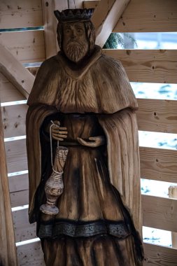 Ayrıntılı bir ahşap oyma, taç takan ve fener tutan, geleneksel zanaatkarlık sergileyen bir kraliyet figürünü tasvir ediyor.