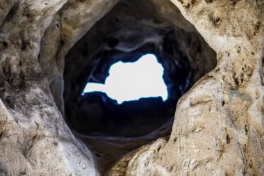 Doğal bir mağaranın kabataslak dokusu karanlığın ötesindeki dünyayı işaret eden parlak bir çıkışı çerçeveler.