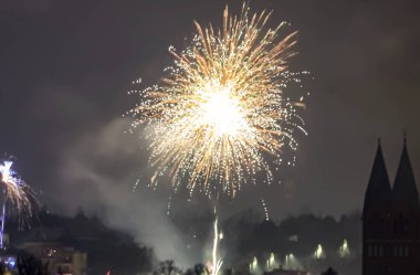 Altın havai fişeklerin muhteşem gösterisi şehir binalarının ve kilise kulesinin üzerindeki karanlık gökyüzünü aydınlatıyor.