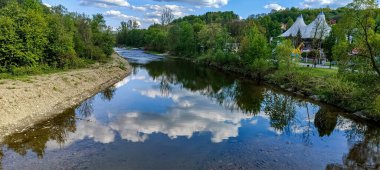 Sakin bir nehir yeşil bir arazide akar, gökyüzünü ve etrafındaki yaprakları yansıtır, uzaktan görülebilen çadırımsı eşsiz bir yapısı vardır.