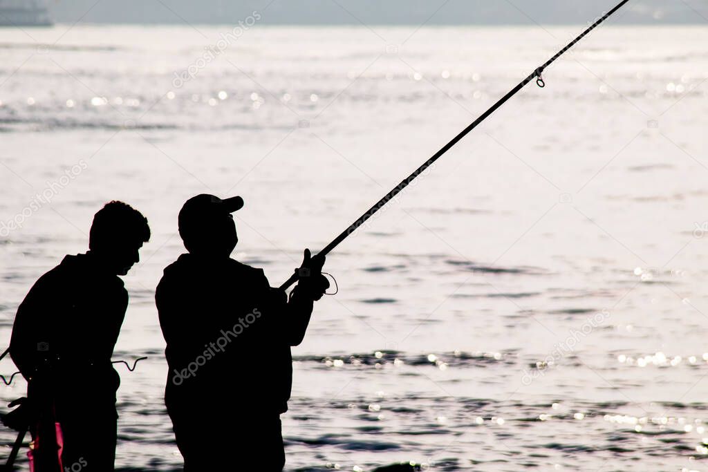 Silhouettes of amateur fishermen with fishing rods on the seashore in early morning time.