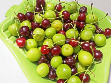 Yeşil bir tabakta meyve figürleriyle ekşi kiraz ve erikleri yemeye ve yıkamaya hazır.