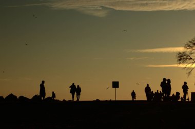 Gün batımında Denizde Yürüyen Siluetler. Huzurlu Akşam Altın Saati Sahnesi. Gün batımında deniz kenarında yürüyen insanlar..