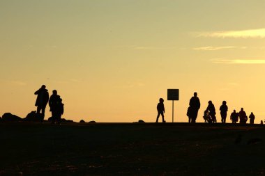 Gün batımında Denizde Yürüyen Siluetler. Huzurlu Akşam Altın Saati Sahnesi. Gün batımında deniz kenarında yürüyen insanlar..