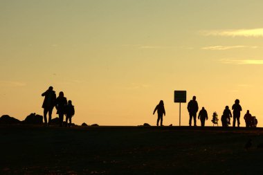 Gün batımında Denizde Yürüyen Siluetler. Huzurlu Akşam Altın Saati Sahnesi. Gün batımında deniz kenarında yürüyen insanlar..