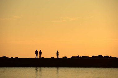 Gün batımında Denizde Yürüyen Siluetler. Huzurlu Akşam Altın Saati Sahnesi. Gün batımında deniz kenarında yürüyen insanlar..