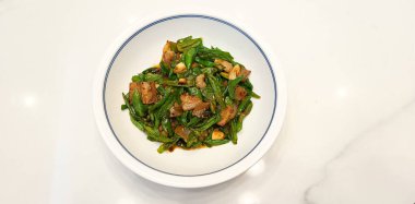 Kızarmış yeşil biber, domuz eti ve sarımsak, beyaz bir seramik kasede servis edilen ev yapımı baharatlı Asya yemeği, Çin mutfağı, baharatlı kızartma, sarımsaklı domuz eti, temiz bir mermer yüzey üzerinde.  