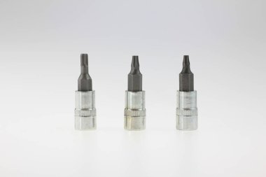 Profesyonel mekanik araçları, dayanıklı aksesuarları, hassas mühendislik ekipmanlarını, endüstriyel donanım parçalarını, otomotiv tamir araçlarını temsil eden beyaz bir stüdyonun arka planında dik duran üç metal tornavida parçası.