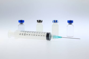 Tıbbî şırınga ile paslanmaz çelik enjeksiyon şırıngası birden fazla ecza cam şişesinin önüne yerleştirilmiş, kapaklarla kapatılmış, lastik tıkaçlar, beyaz arka planda izole edilmiş. Aşılar, ilaçlar, insülin, antibiyotikler için laboratuvarda ve hastanelerde,