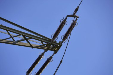 Yüksek voltajlı elektrik iletim hatları ve kuleler açık bir gökyüzünün altında peyzaj boyunca uzanıyor. Görüntü enerji dağılımı, güç altyapısı, elektrik arzı, sanayi ve modern teknolojiyi temsil etmektedir. Konseptler için uygun