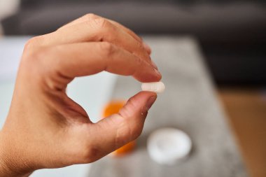 Elinde tutulan turuncu bir hap şişesinin yakın plan fotoğrafı. Tabletler konteynırın içinde ve etrafına saçılmış. İlaç, sağlık sigortası, ilaç, vitamin, tedavi ve tıbbi güvenlik kavramı. Sağlığa uygun temiz, minimal bileşim