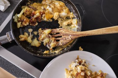 Çırpılmış yumurta, dökme demir tavada pişiyor. Geleneksel bir tavada hazırlanmış ev yapımı kahvaltı. Yemek pişirme, konfor yemeği, ev yemeği, kahvaltı ve basit mutfak kavramı. Sıcak tonlar ve otantik mutfak atmosferi.