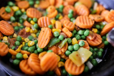 Cooked vegetables in a skillet, including carrots, peas, and fresh herbs. Concept of healthy eating, vegetarian meal, home cooking, nutritious food, and simple cuisine. Colorful and fresh presentation, suitable for food, lifestyle, and recipe content