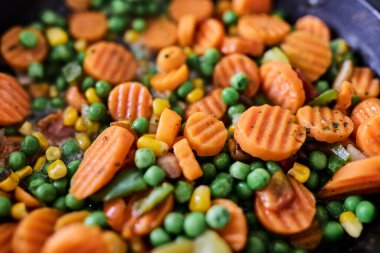 İçinde havuç, bezelye ve taze bitkiler bulunan bir tavada pişmiş sebze. Sağlıklı beslenme, vejetaryen yemeği, ev yemeği, besleyici yemek ve basit mutfak kavramı. Renkli ve taze sunum, yemek, yaşam tarzı ve tarif içeriği için uygun