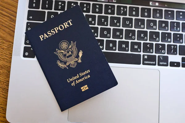 Tahta bir masada, açık bir dizüstü bilgisayar ve deri bir cüzdanın yanında yatan bir Amerikan pasaportu. Seyahat belgeleri ve kişisel aksesuarlar düz konumda dizilmiş. İş seyahati, uluslararası seyahat hazırlığı, kimlik ve güvenlik kavramı.