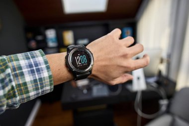 İnsan bileğine takılmış modern bir ukalanın yakın plan görüntüsü. Cihaz parlak bir tasarım ve dijital arayüzü, akıllı teknolojiyi, giyilebilir cihazları, sağlık takibi, fitness izleme ve modern yaşam tarzını sembolize eder. Yenilik kavramı