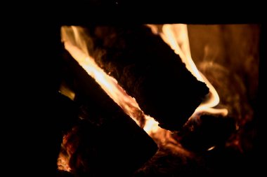 Eski bir sobanın içinde parlayan kömürlerin ve yanan odunların yakın görüntüsü. Görüntü sıcaklık, sıcaklık ve kırsal bir atmosfer taşır. Geleneksel ısıtma, yangın, enerji, kış konforu, kırsal yaşam ve klasik ev iç mimarisi kavramı.