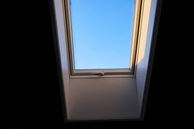 Tavana monte edilmiş bir çatı penceresi doğal ışığın boşluğa girmesine olanak sağlıyor. Görüntü modern mimariyi, iç tasarımı ve parlak yaşam alanlarını temsil eder. Doğal ışıklandırma kavramı, ev dekorasyonu, çağdaş tasarım ve konforlu.