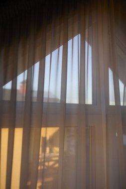 Kış günü, sıcak bir tavan arasında güneş ışığıyla aydınlanan perdeler. Görüntü, sıcaklığı, doğal ışığı ve yerleşim yerlerinde sakin bir atmosferi iletir. Ev dekorasyonu, çatı katında yaşama, kış güneşi ve huzur.