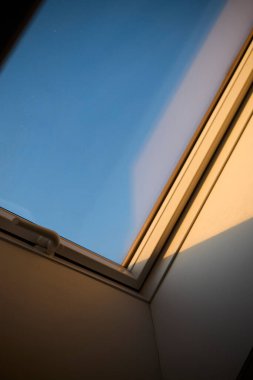 Tavana monte edilmiş bir çatı penceresi doğal ışığın boşluğa girmesine olanak sağlıyor. Görüntü modern mimariyi, iç tasarımı ve parlak yaşam alanlarını temsil eder. Doğal ışıklandırma kavramı, ev dekorasyonu, çağdaş tasarım ve konforlu.