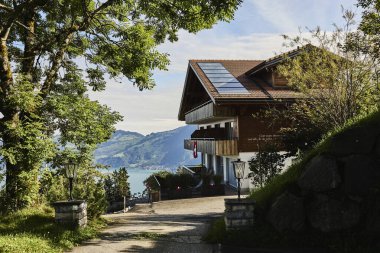 Geleneksel İsviçre dağ evi tarzı otel, yaz mevsiminde gün ışığında görkemli dağların ve huzurlu bir alp gölünün zeminine karşı ele geçirildi. Görüntü seyahat, konukseverlik ve İsviçre Alplerinin doğal güzelliğini temsil ediyor.