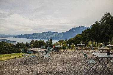 Yazın İsviçre 'de Alp Dağları' na bakan bir otelin yakınındaki açık masa ve sandalyeler. Görüntü seyahat, konukseverlik, rahatlama ve açık hava yemeklerini temsil ediyor. Yaz tatili kavramı, turizm, boş zaman ve...