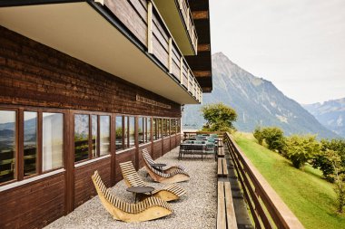 Geleneksel İsviçre dağ evi tarzı otel, yaz mevsiminde gün ışığında görkemli dağların ve huzurlu bir alp gölünün zeminine karşı ele geçirildi. Görüntü seyahat, konukseverlik ve İsviçre Alplerinin doğal güzelliğini temsil ediyor.