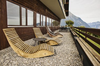 Yazın İsviçre 'de Alp Dağları' na bakan bir otelin yakınındaki açık masa ve sandalyeler. Görüntü seyahat, konukseverlik, rahatlama ve açık hava yemeklerini temsil ediyor. Yaz tatili kavramı, turizm, boş zaman ve...