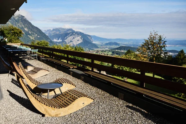 Yazın İsviçre 'de Alp Dağları' na bakan bir otelin yakınındaki açık masa ve sandalyeler. Görüntü seyahat, konukseverlik, rahatlama ve açık hava yemeklerini temsil ediyor. Yaz tatili kavramı, turizm, boş zaman ve...