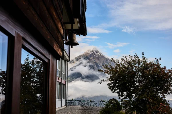 Yemek sandalyeleri İsviçre 'de bir dağ otelinin yanında, sonbahar renklerinde, karla kaplı Alpler' in arka planında. Sahne rahat bir konukseverlik, dağlık bir ortam ve mevsimlik güzelliği temsil ediyor. Seyahat ve açık hava yemekleri için uygun.