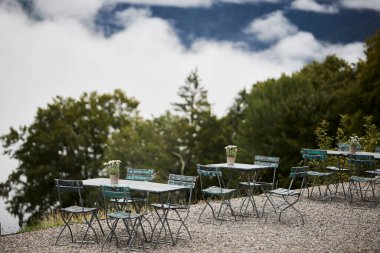 İsviçre 'de bir dağ otelinin terasında taze Edelweiss çiçekleriyle süslenmiş abur cubur masaları. Sahne alp misafirperverliğini, açık hava yemeklerini ve manzaralı bir dağ atmosferini yansıtıyor. Seyahat, eğlence ve otel kavramları için uygundur.