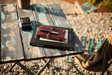 İsviçre 'de bir yaz akşamı manzaralı dağ manzaralı bir terasta sandalye ve masa. Sandalyede sıcak bir eşarp, deri bir seyahat çantası, bir defter ve masanın üzerinde Edelweiss çiçekleri olan bir kamera var. Sahne rahatlatıcı.