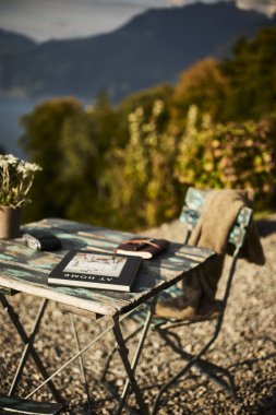 İsviçre 'de bir yaz akşamı manzaralı dağ manzaralı bir terasta sandalye ve masa. Sandalyede sıcak bir eşarp, deri bir seyahat çantası, bir defter ve masanın üzerinde Edelweiss çiçekleri olan bir kamera var. Sahne rahatlatıcı.
