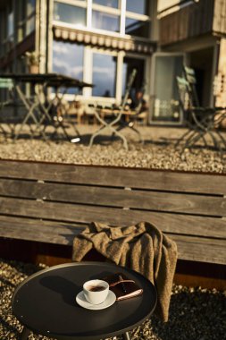 İsviçre 'de bir yaz akşamı manzaralı dağ manzaralı bir terasta sandalye ve masa. Sandalyede sıcak bir eşarp, deri bir seyahat çantası, bir defter ve bir kamera, bir fincan kahve ve Edelweiss çiçekleri masanın üzerinde otururken,