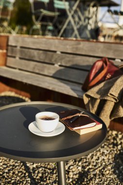 İsviçre 'de bir yaz akşamı manzaralı dağ manzaralı bir terasta sandalye ve masa. Sandalyede sıcak bir eşarp, deri bir seyahat çantası, bir defter ve bir kamera, bir fincan kahve ve Edelweiss çiçekleri masanın üzerinde otururken,