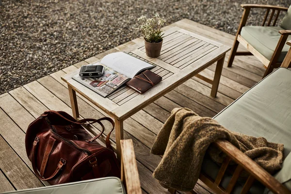 İsviçre 'de bir yaz akşamı manzaralı dağ manzaralı bir terasta sandalye ve masa. Sandalyede sıcak bir eşarp, deri bir seyahat çantası, bir defter ve masanın üzerinde Edelweiss çiçekleri olan bir kamera var. Sahne rahatlatıcı.