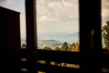 İsviçre yazında dağ manzaralı sandalyeler, çay, kahve ve kitapların yer aldığı bir otel balkonu ve göl manzarası. Sahne, rahat bir dağlık yaşam tarzı, huzurlu bir atmosfer ve rahat bir seyahat deneyimi yakalıyor. Konseptler için uygun
