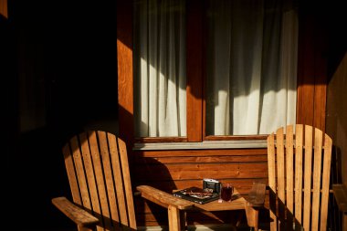 İsviçre yazında dağ manzaralı sandalyeler, çay, kahve ve kitapların yer aldığı bir otel balkonu ve göl manzarası. Sahne, rahat bir dağlık yaşam tarzı, huzurlu bir atmosfer ve rahat bir seyahat deneyimi yakalıyor. Konseptler için uygun