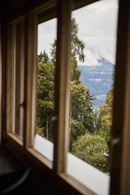 İsviçre yazında dağ manzaralı sandalyeler, çay, kahve ve kitapların yer aldığı bir otel balkonu ve göl manzarası. Sahne, rahat bir dağlık yaşam tarzı, huzurlu bir atmosfer ve rahat bir seyahat deneyimi yakalıyor. Konseptler için uygun
